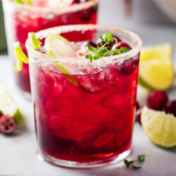 Two cold Cran-Raz Margaritas with salted rims and lime